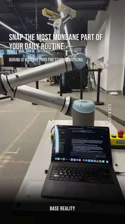 Base Reality mission 23, "Snap the most mundane part of your daily routine.", answered with an industrial robot arm beside a laptop on a lab bench.